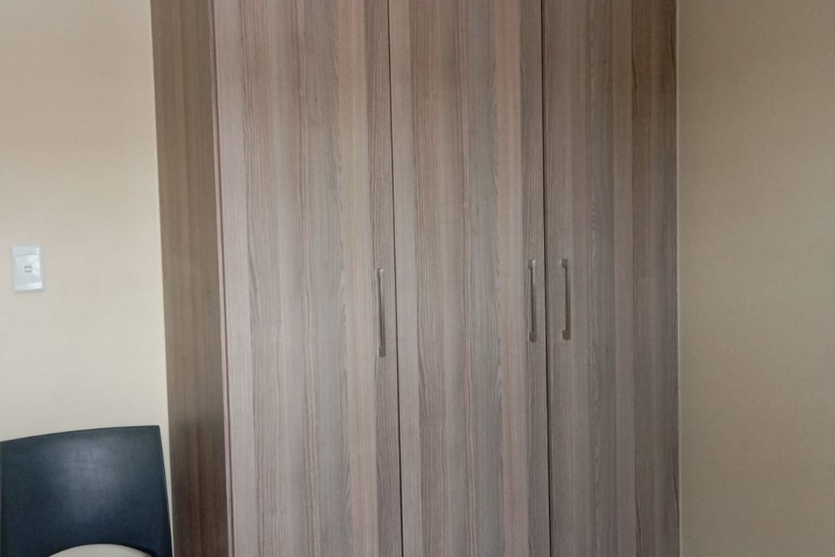 A bedroom featuring built-in wooden cupboards with modern handles, providing ample storage space.