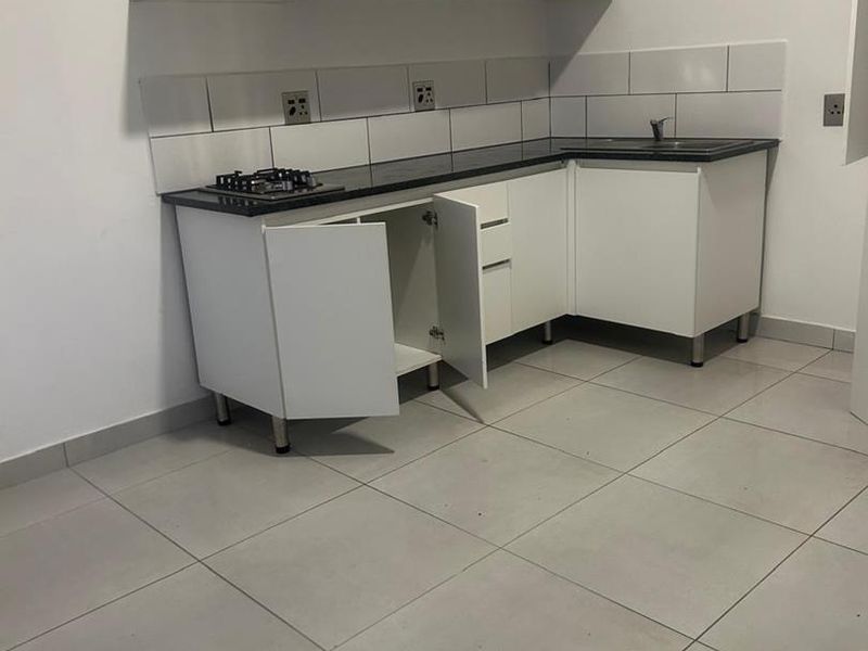 A compact, empty kitchen featuring white cabinetry, a dark countertop, gas hob, and tiled backsplash, ready for personalization.