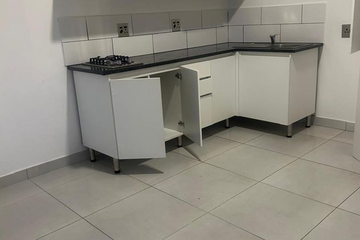 A compact, empty kitchen featuring white cabinetry, a dark countertop, gas hob, and tiled backsplash, ready for personalization.