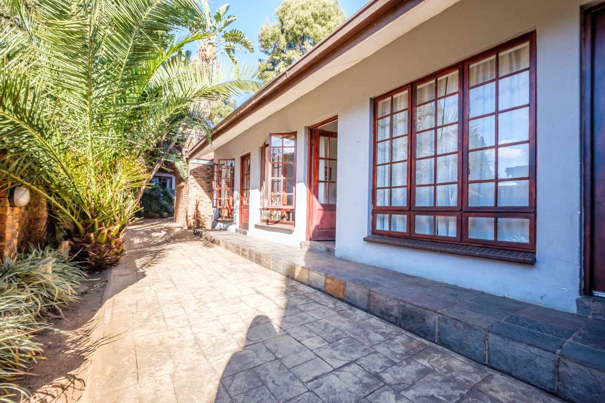 A rear exterior view of the guest house featuring a paved patio area, timber-framed windows, and doors leading into the building.