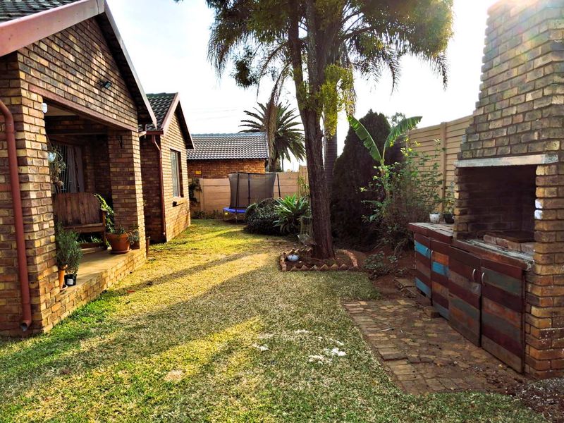 Rear garden area featuring a covered patio, lawn, and a built-in brick braai facility, providing a functional outdoor entertainment space.