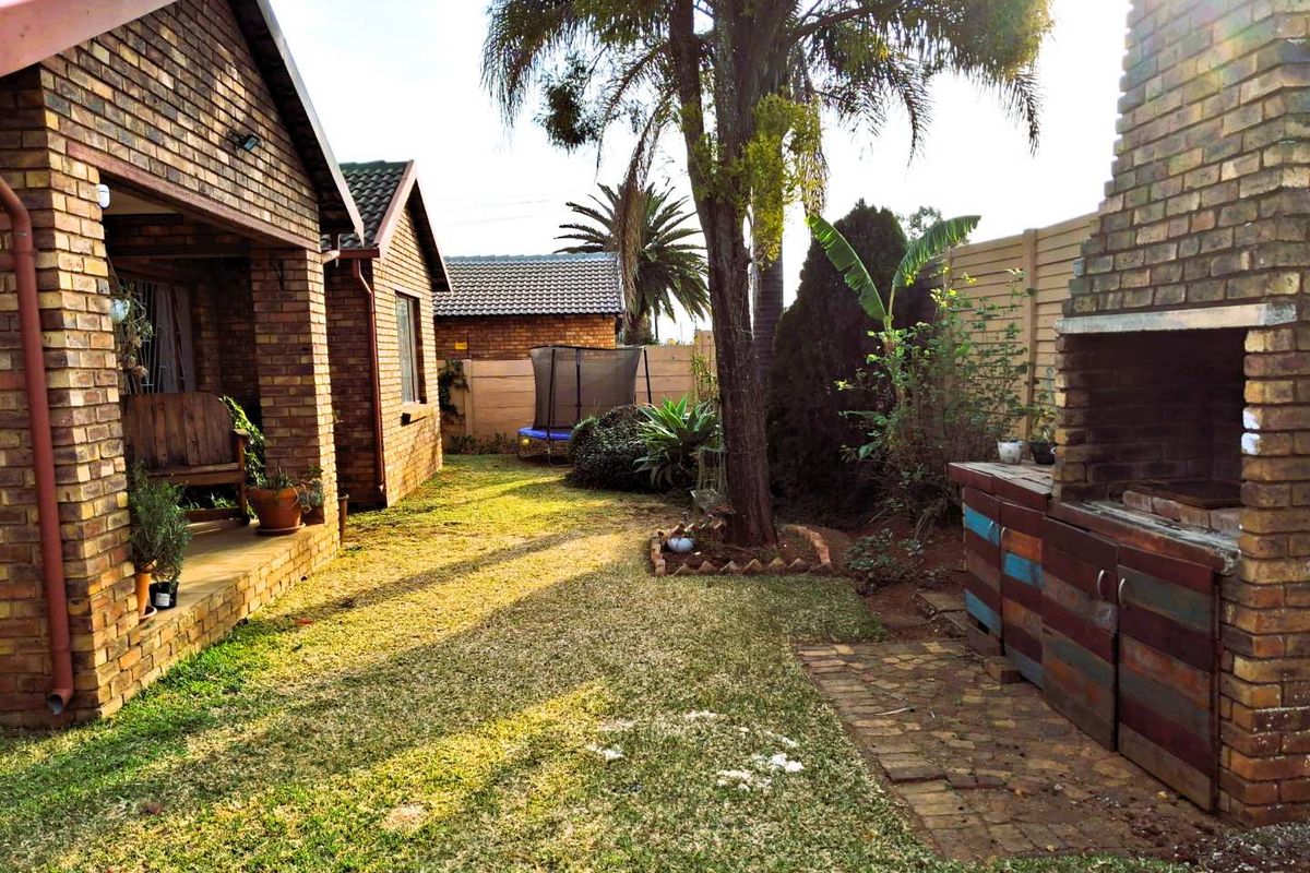 Rear garden area featuring a covered patio, lawn, and a built-in brick braai facility, providing a functional outdoor entertainment space.