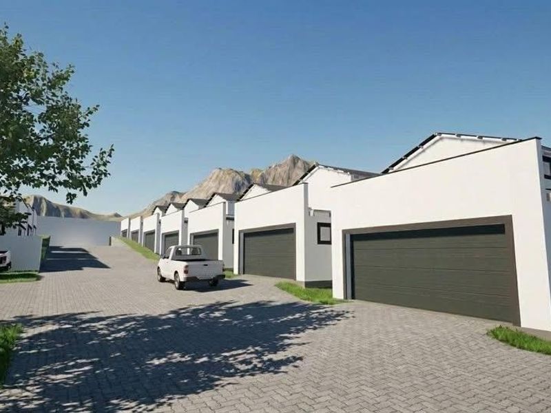 A row of modern townhouse units featuring paved driveways and sectional garage doors, set against a scenic mountain backdrop.