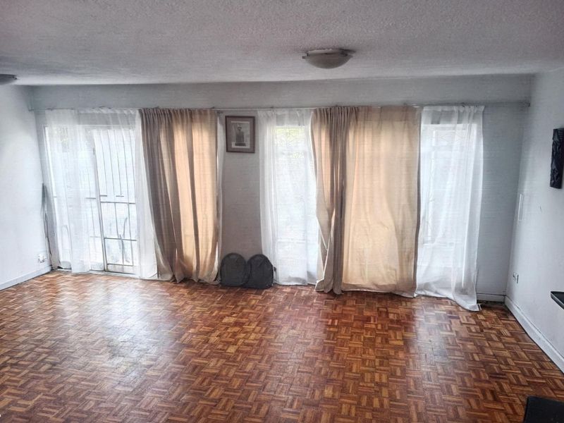 Spacious living area featuring original parquet flooring and large sliding glass doors with security gates, offering ample natural light.