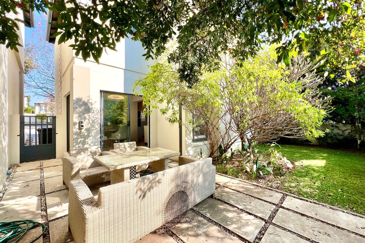 A private rear garden featuring a paved patio area, established trees, and direct access to the interior living space through sliding glass doors.