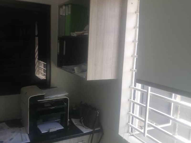 A functional office space featuring built-in cabinetry, a desk, and a window fitted with security bars and a roller blind.