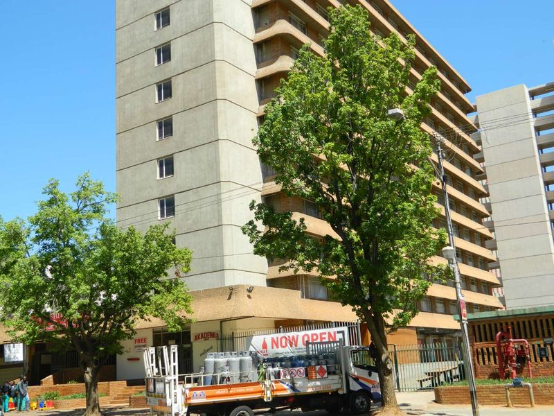 Exterior view of a multi-story apartment building featuring a concrete facade with balconies and perimeter security fencing.