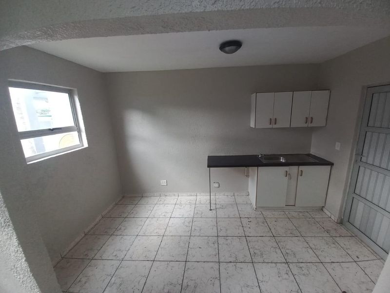 A compact, empty kitchen area featuring basic built-in cabinetry, a stainless steel sink, and tiled flooring, ready for renovation or modernization.