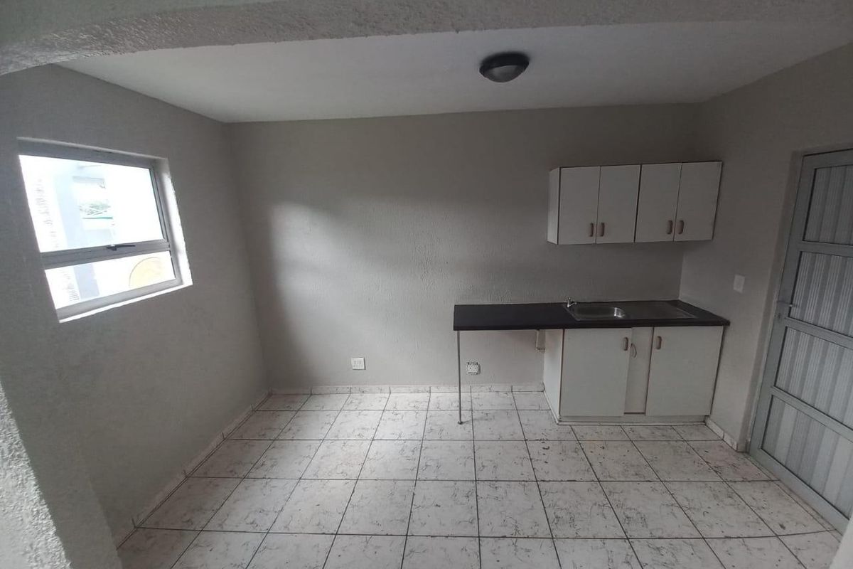 A compact, empty kitchen area featuring basic built-in cabinetry, a stainless steel sink, and tiled flooring, ready for renovation or modernization.