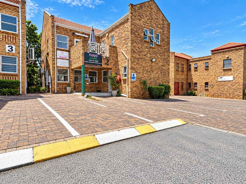 Exterior view of a multi-unit commercial brick building featuring a paved parking lot, covered parking bays, and prominent business signage.