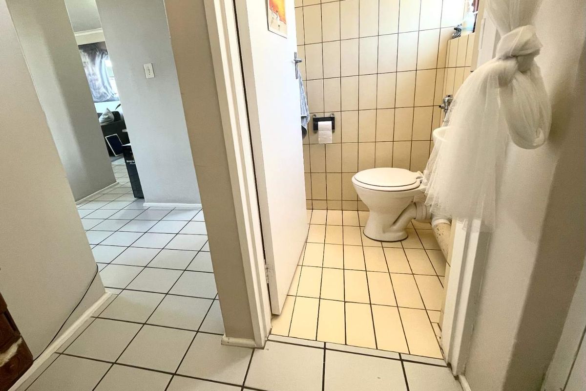 A compact bathroom featuring tiled walls and flooring, equipped with a standard toilet and pedestal basin, requiring cosmetic updates to improve its overall condition.