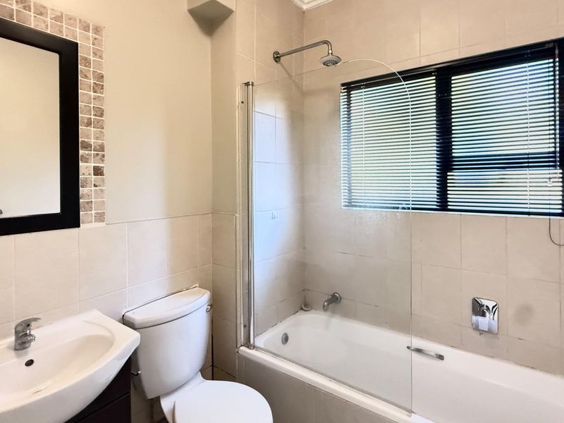A functional bathroom featuring a bathtub with a glass shower screen, a wall-mounted basin, and a toilet, finished with neutral wall tiles.