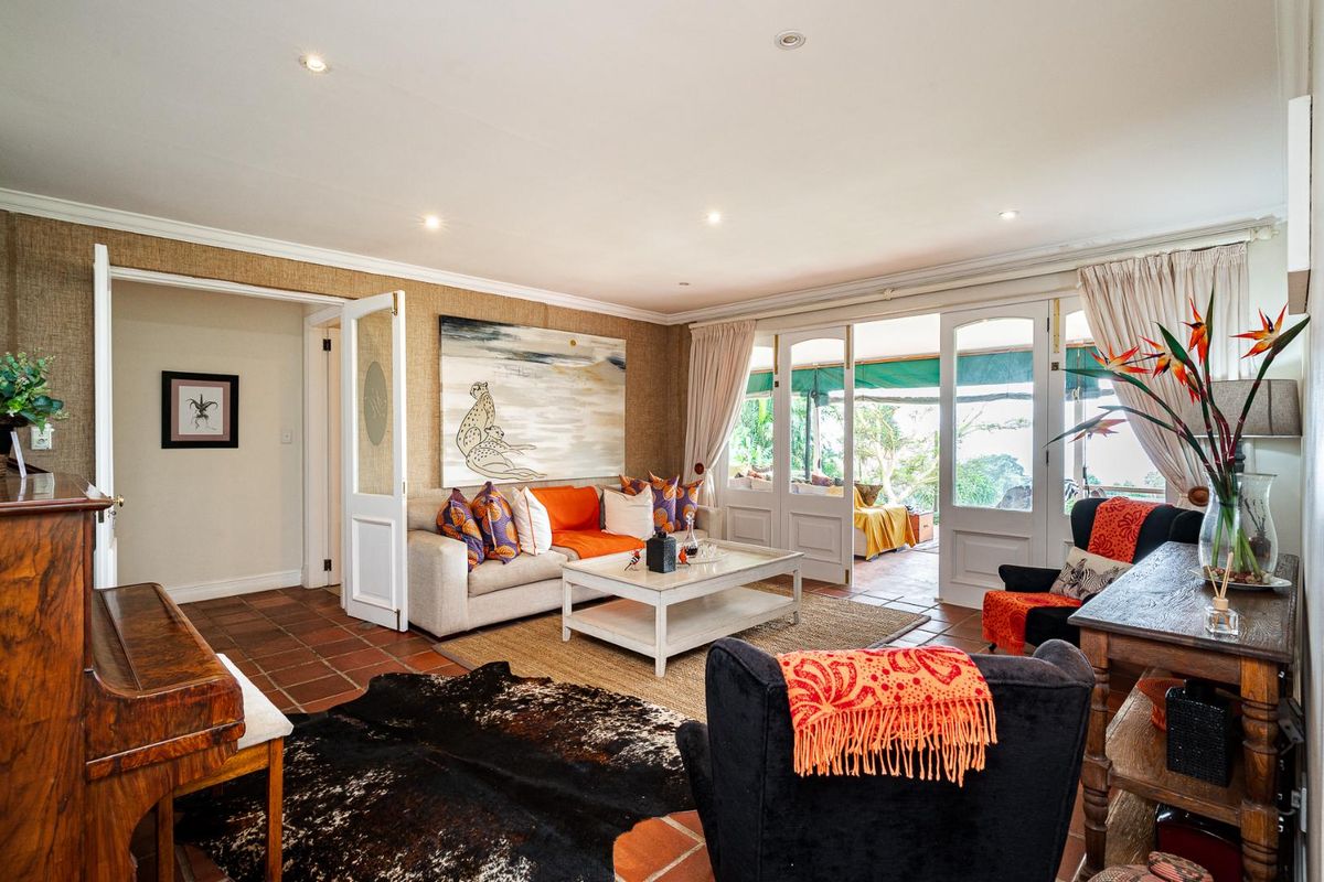 A spacious living room featuring terracotta floor tiles, textured wallpaper, and double french doors providing seamless access to the outdoor patio area.