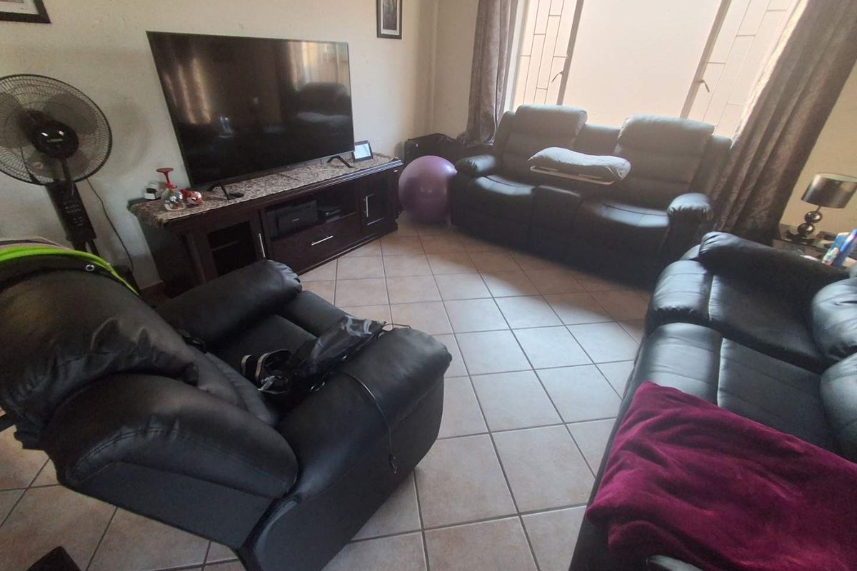 A living room featuring tiled flooring and a large window with security bars, providing a functional space for relaxation.