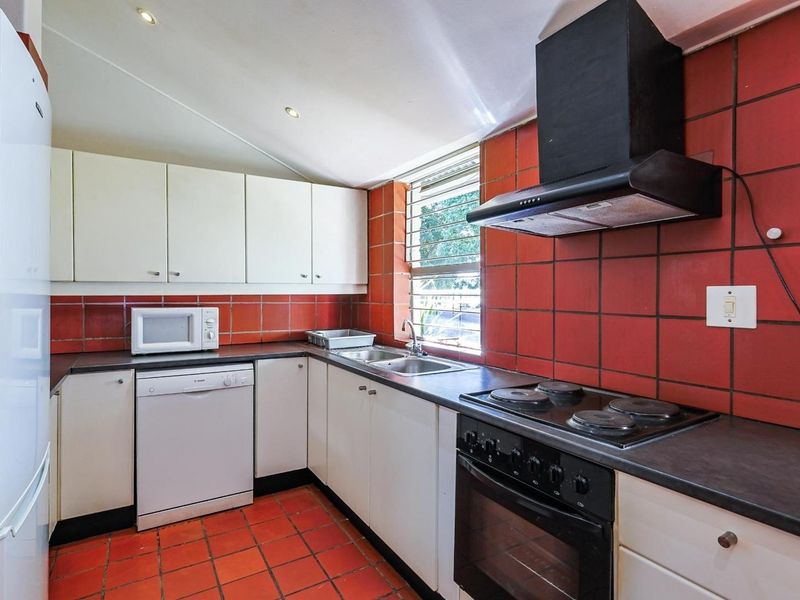 Functional kitchen featuring white cabinetry, dark countertops, integrated electric hob and oven, extractor fan, and distinctive red tiled splashback and flooring.