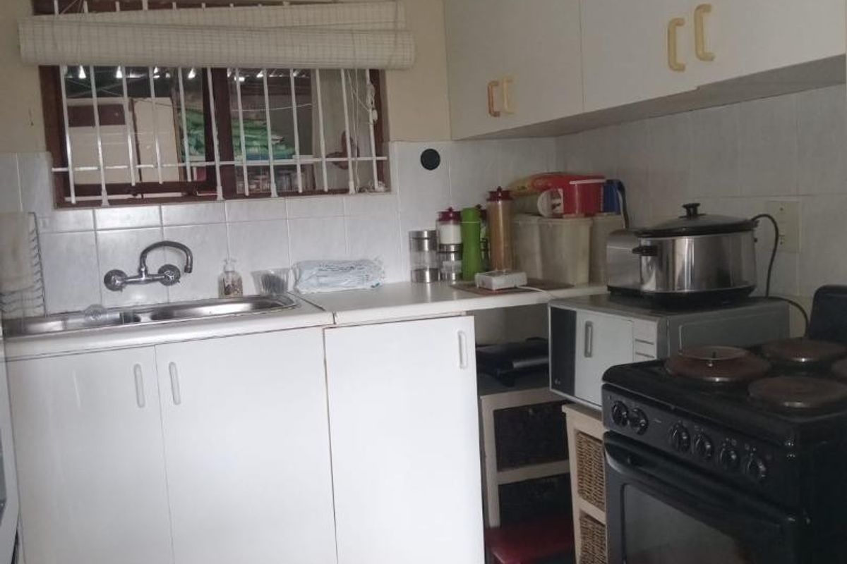 A compact kitchen featuring white laminate cabinetry, tiled flooring, and a tiled backsplash, offering a functional layout with potential for modern updates.
