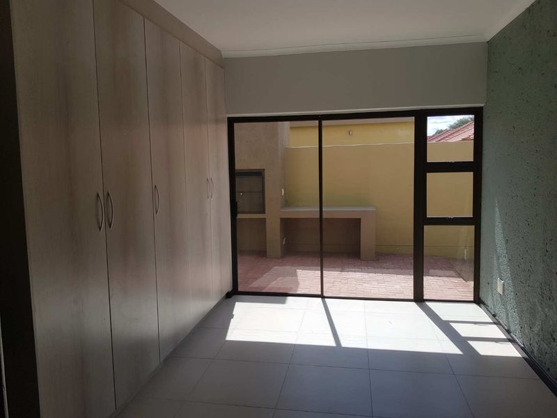 A bright, empty bedroom featuring modern built-in cupboards, tiled flooring, and a sliding glass door providing direct access to a private patio area.