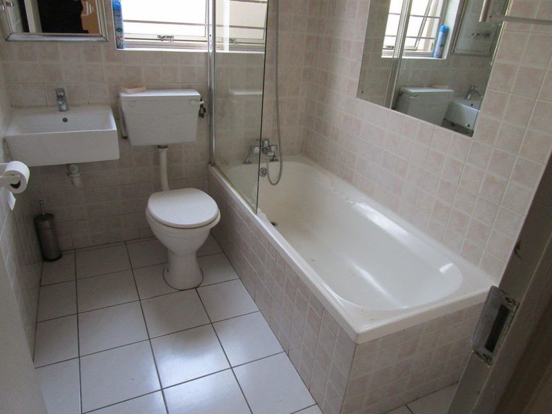 A functional bathroom featuring a bathtub with a glass screen, wall-mounted basin, and toilet, finished with tiled walls and flooring.