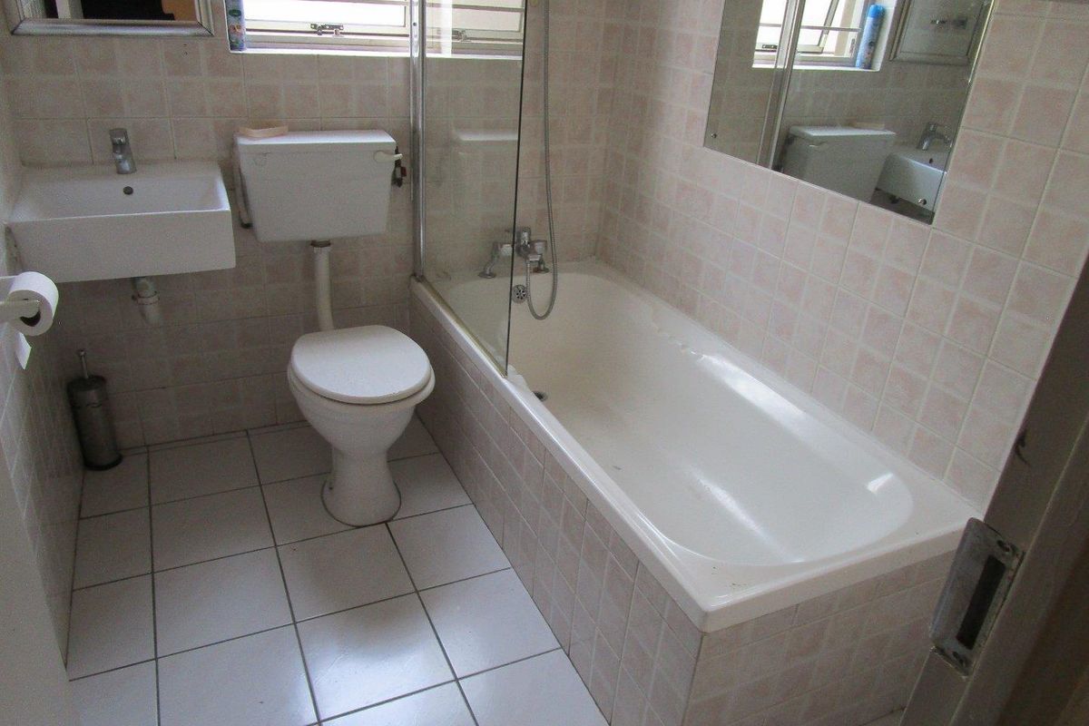 A functional bathroom featuring a bathtub with a glass screen, wall-mounted basin, and toilet, finished with tiled walls and flooring.