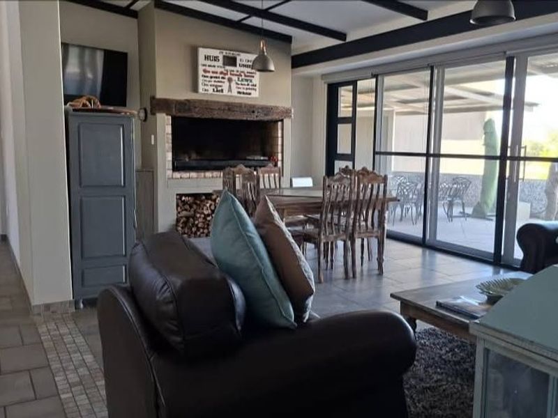 Spacious open-plan living and dining area featuring a built-in fireplace, exposed ceiling beams, and large sliding glass doors leading to an outdoor patio.