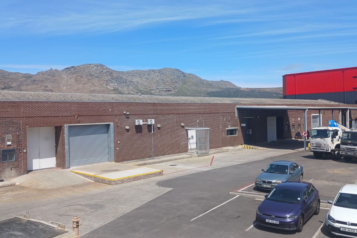 Rear industrial exterior featuring a brick facade, loading dock with roller shutter door, and paved yard area with mountain views.