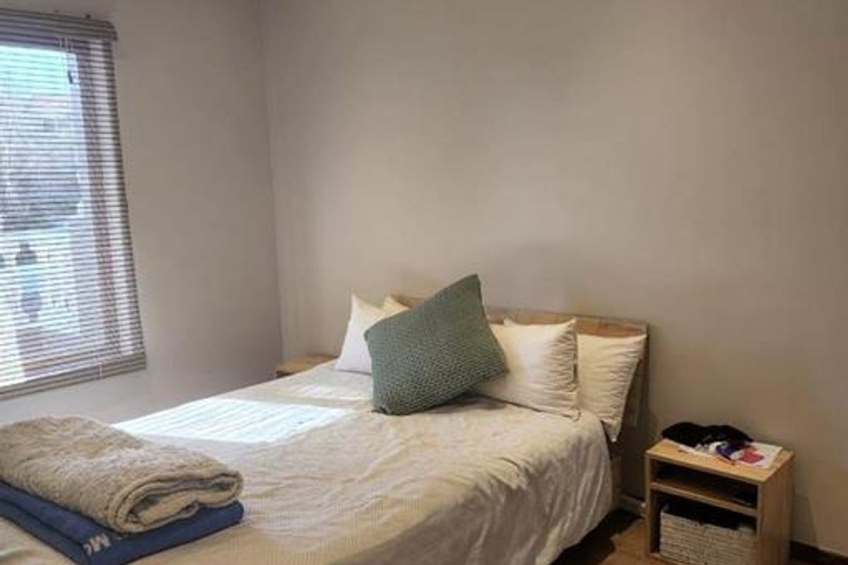A well-maintained bedroom featuring laminate flooring, recessed ceiling lighting, and a ceiling fan, with natural light provided by a window with venetian blinds.