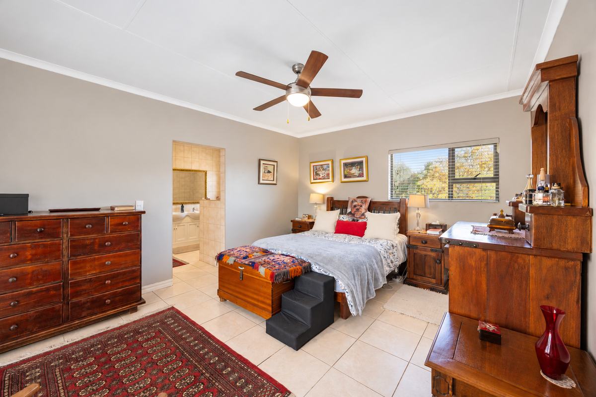 Spacious bedroom featuring tiled flooring, a ceiling fan, and direct access to an en-suite bathroom with neutral wall finishes.