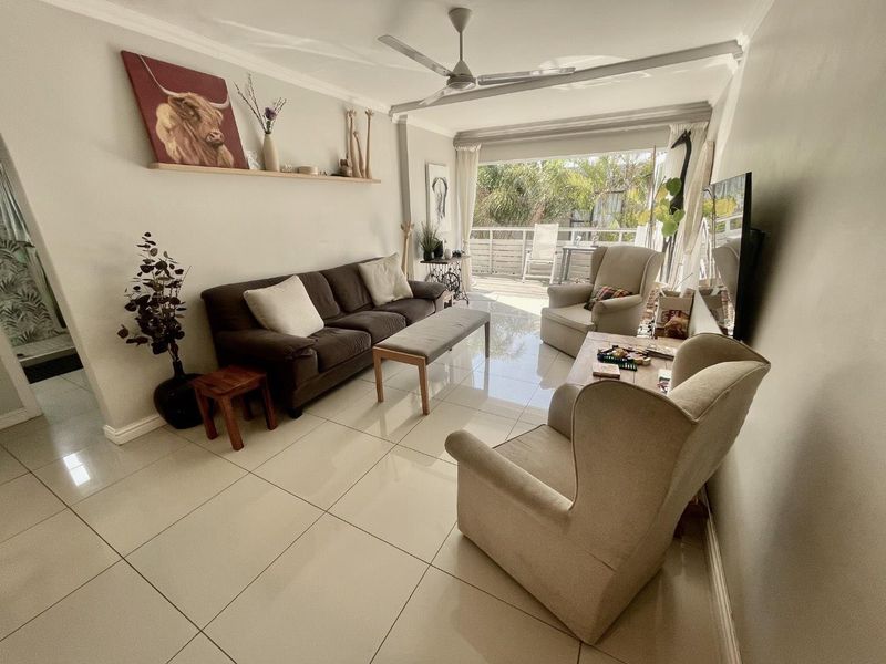 A bright living room featuring large format floor tiles, a ceiling fan, and sliding glass doors that open onto an outdoor patio area.