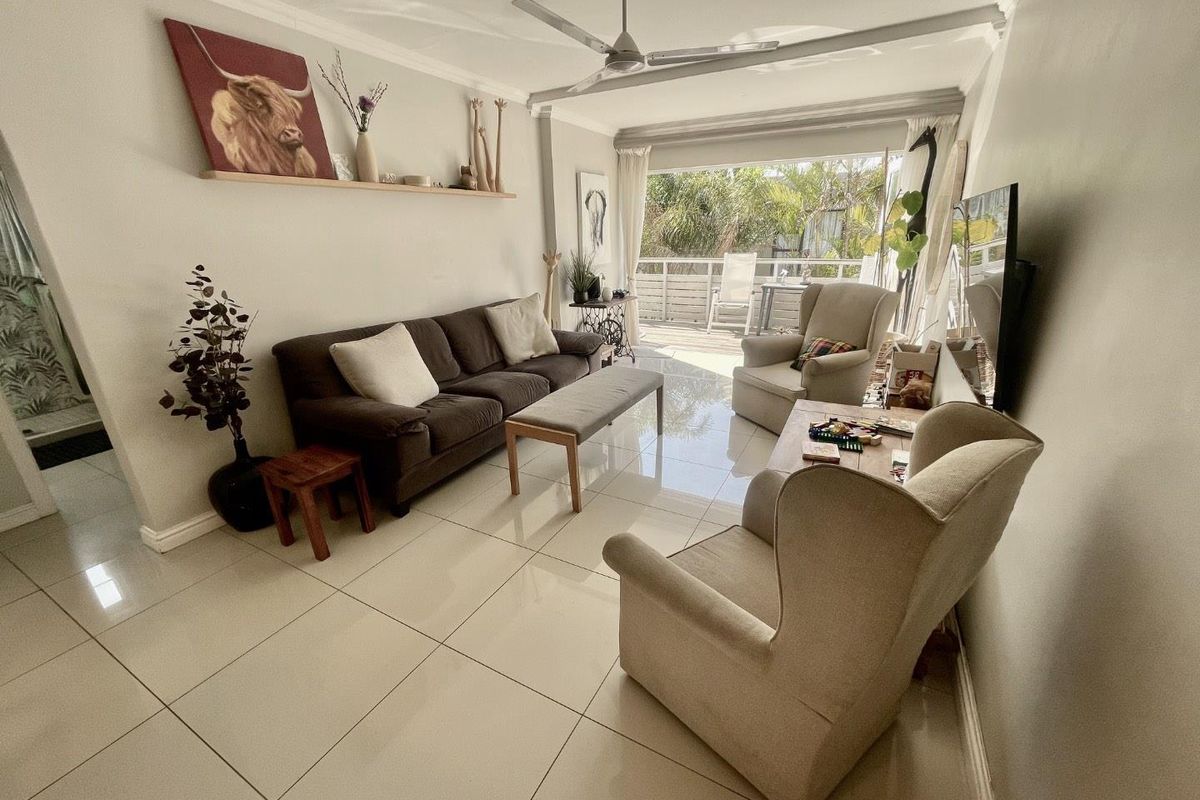 A bright living room featuring large format floor tiles, a ceiling fan, and sliding glass doors that open onto an outdoor patio area.