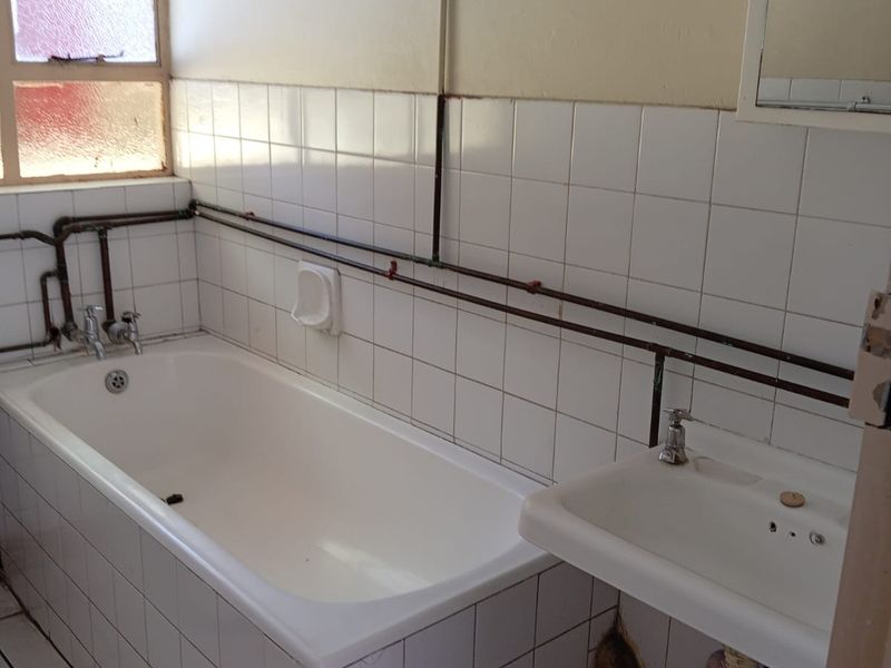A dated bathroom featuring a bathtub, wall-mounted basin, and exposed plumbing, requiring modernization and cosmetic updates to improve functionality and aesthetic appeal.