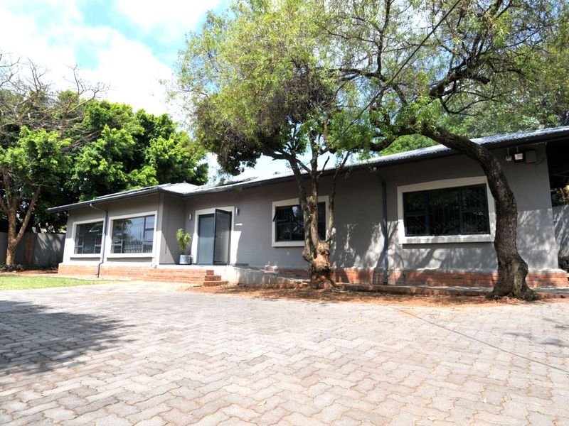 Front exterior view of a commercial property featuring a paved driveway, ramp access, and a grey facade with security-fitted windows.