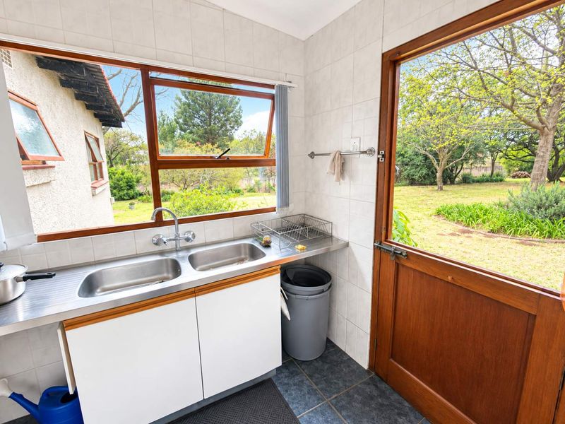 A functional scullery area featuring a double stainless steel sink, tiled splashbacks, and direct access to the garden through a timber framed door.