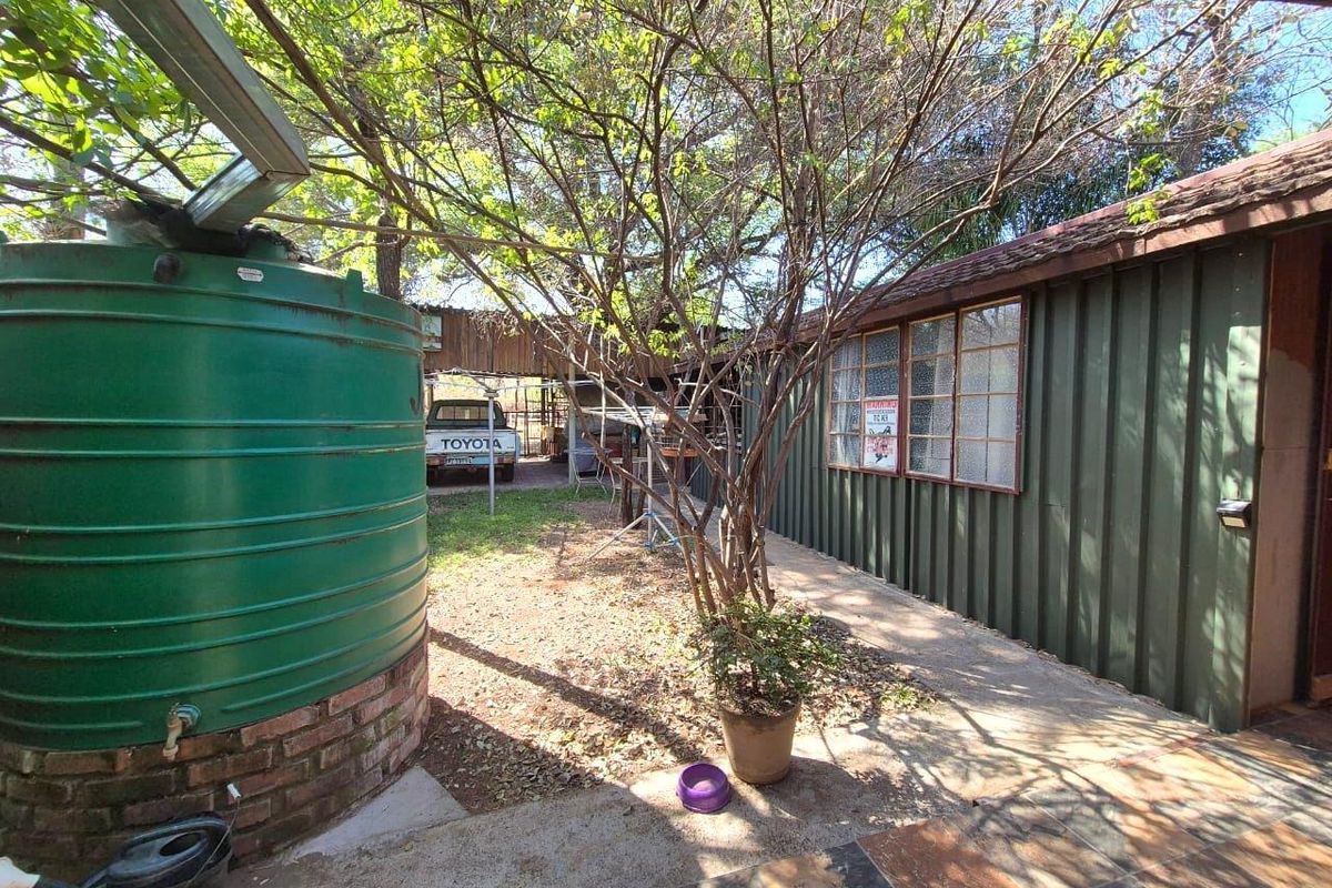 Rear exterior view featuring a large water tank, metal-clad wall, and paved walkway leading to a covered parking area.