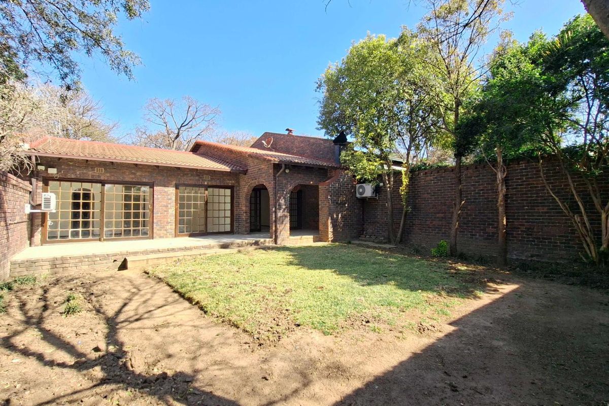 Rear view of the townhouse featuring a brick facade, covered patio area, sliding glass doors, and a private garden with a brick boundary wall.