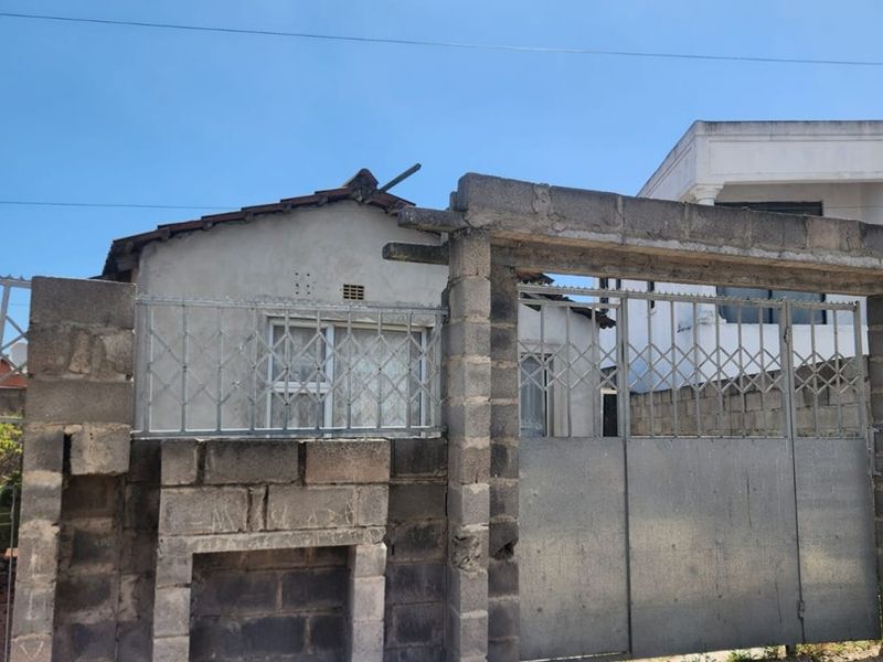 Front view of a residential property featuring a concrete block boundary wall and metal security gate, showing signs of significant weathering and unfinished construction.