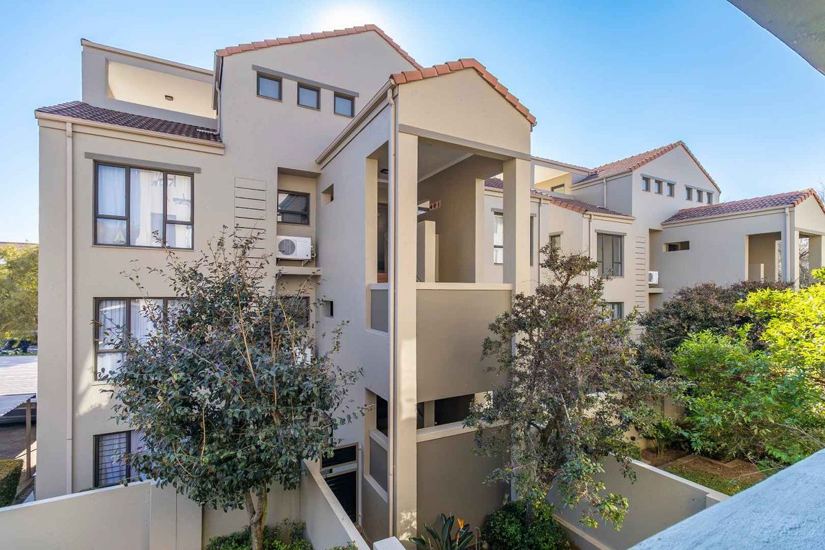 A view of the rear elevation of a multi-story apartment complex featuring terracotta roof tiles, stucco walls, and private balconies.