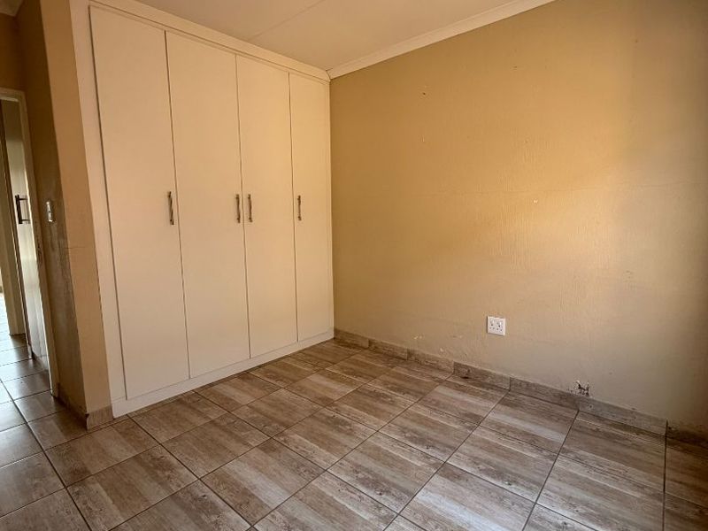 An empty bedroom featuring tiled flooring, built-in cupboards, and neutral wall finishes, offering a blank canvas for personalization.