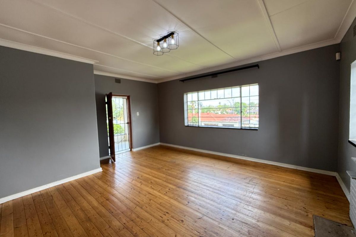 Spacious living area featuring polished hardwood flooring, neutral grey walls, and a large steel-framed window providing natural light.