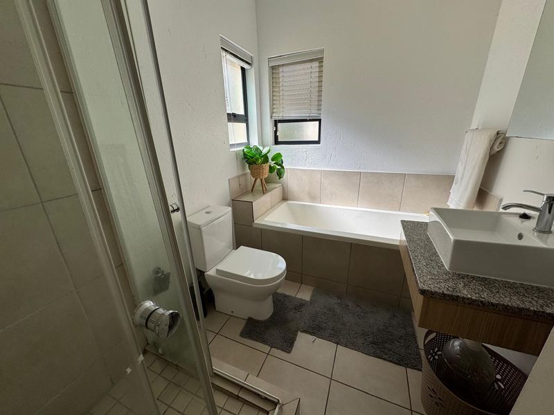 A functional bathroom featuring a built-in bathtub, glass shower enclosure, vessel sink on a granite vanity, and neutral tiled finishes.