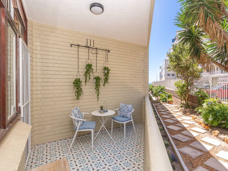 A well-maintained ground-floor balcony featuring decorative patterned floor tiles, a painted brick wall, and a metal balustrade overlooking a landscaped garden area.