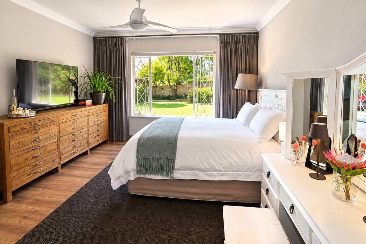 A well-maintained bedroom featuring laminate flooring, crown molding, a ceiling fan, and large windows with security bars overlooking the garden.