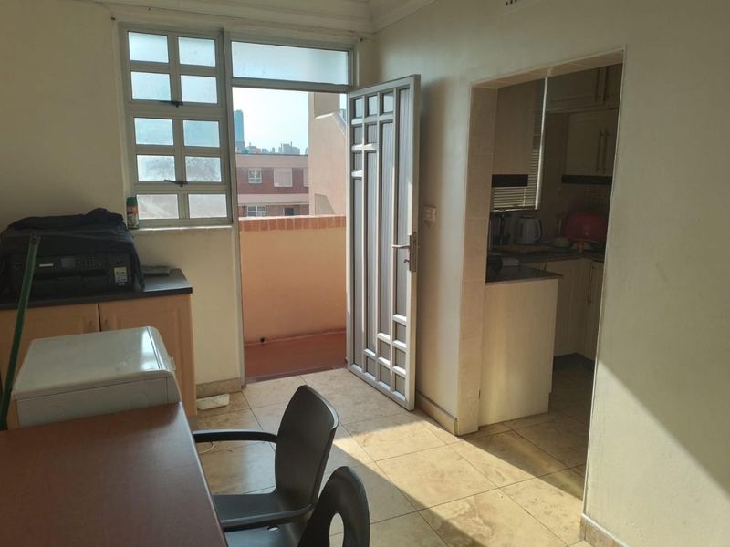 Open plan living area featuring tiled floors, a security gate leading to a balcony, and an adjacent kitchen space.