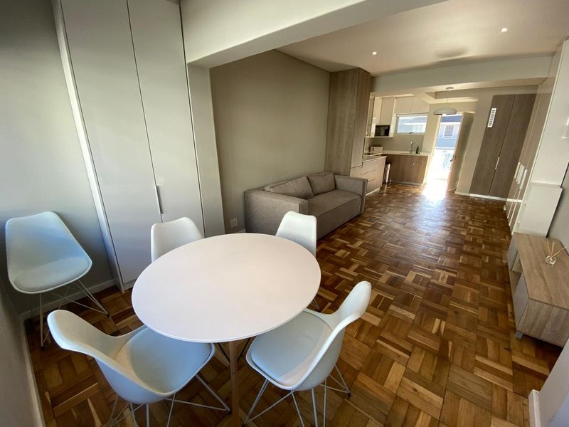 Open-plan living and dining area featuring classic parquet flooring, neutral walls, and a modern kitchen with integrated cabinetry.