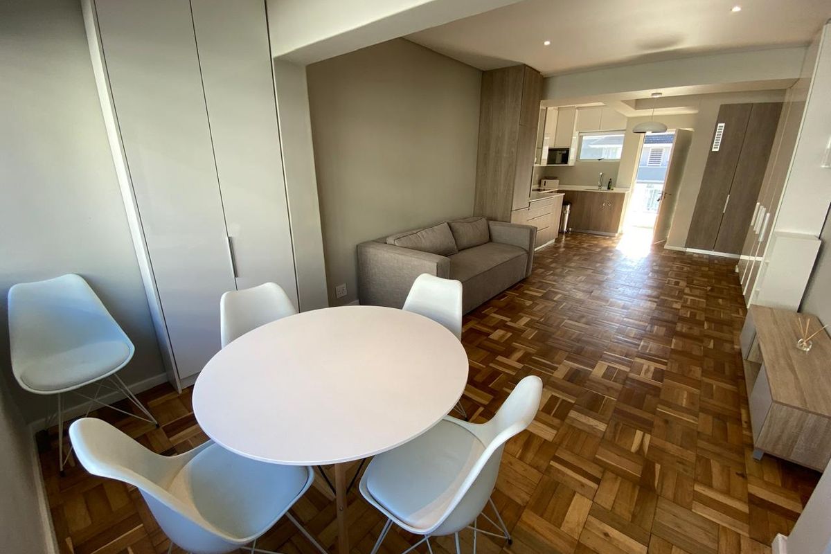 Open-plan living and dining area featuring classic parquet flooring, neutral walls, and a modern kitchen with integrated cabinetry.