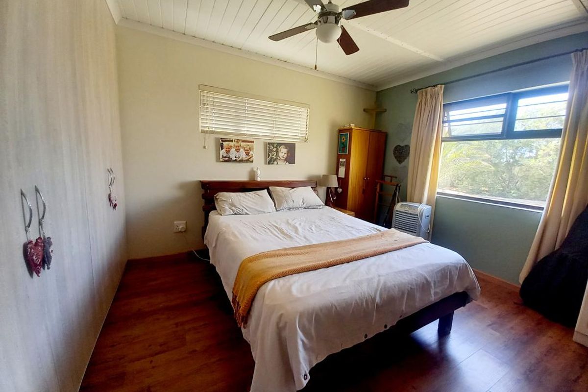 A bedroom featuring wood-look laminate flooring, a ceiling fan, and built-in cupboards, with natural light provided by a window with blinds.
