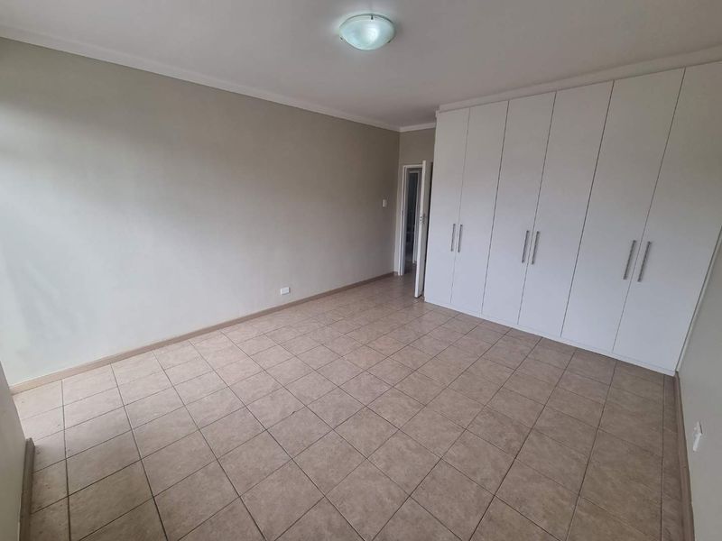 A spacious, empty bedroom featuring neutral tiled flooring and extensive built-in white cupboards, offering a clean and versatile living space.
