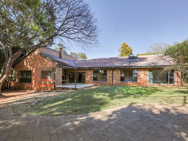 Rear view of a single-story brick house featuring a paved patio, built-in braai, solar water heater, and a spacious garden area.