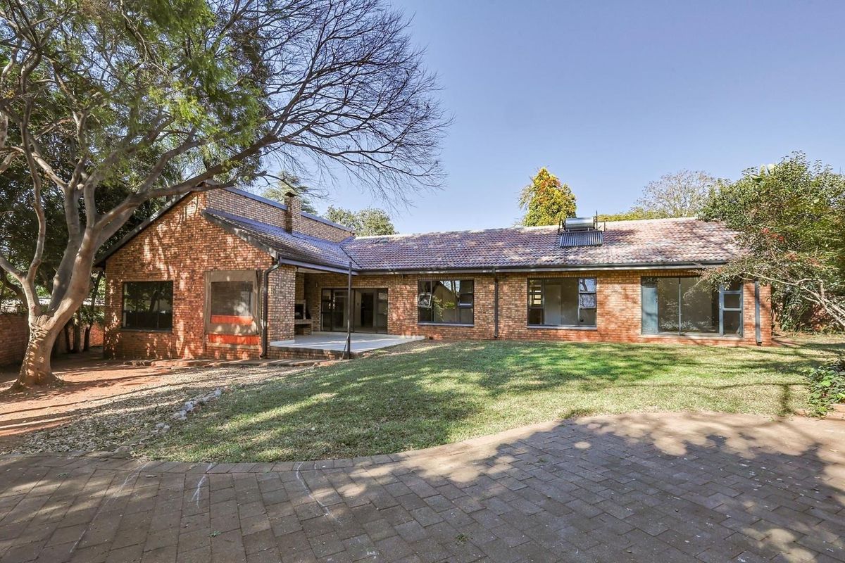 Rear view of a single-story brick house featuring a paved patio, built-in braai, solar water heater, and a spacious garden area.