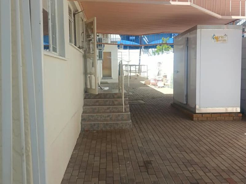 A paved outdoor patio area featuring a covered roof structure, external stairs, and a secure entrance, providing a functional transition space.