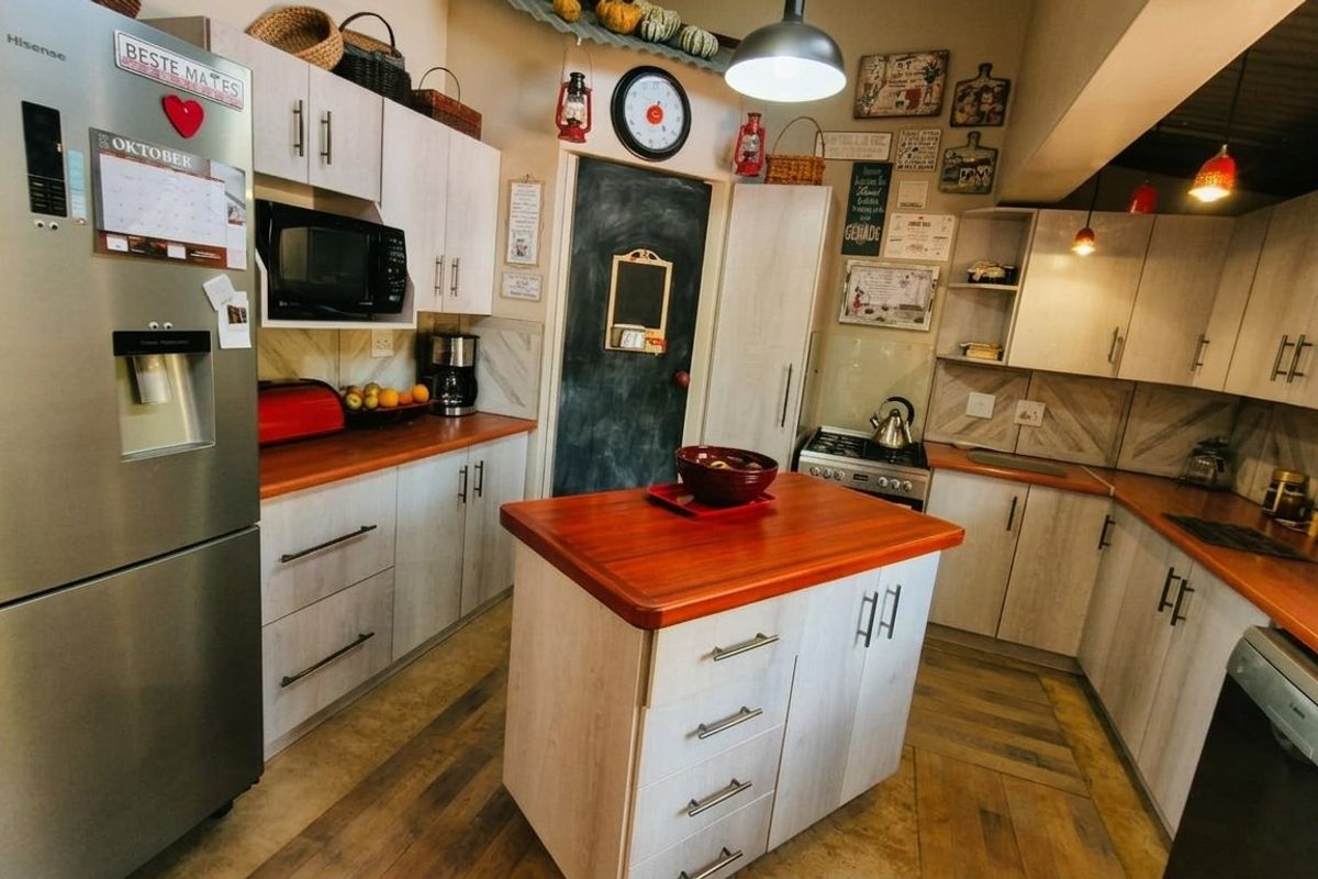 A functional kitchen featuring light-toned cabinetry, warm wooden countertops, a central island, and integrated appliances with a tiled backsplash.